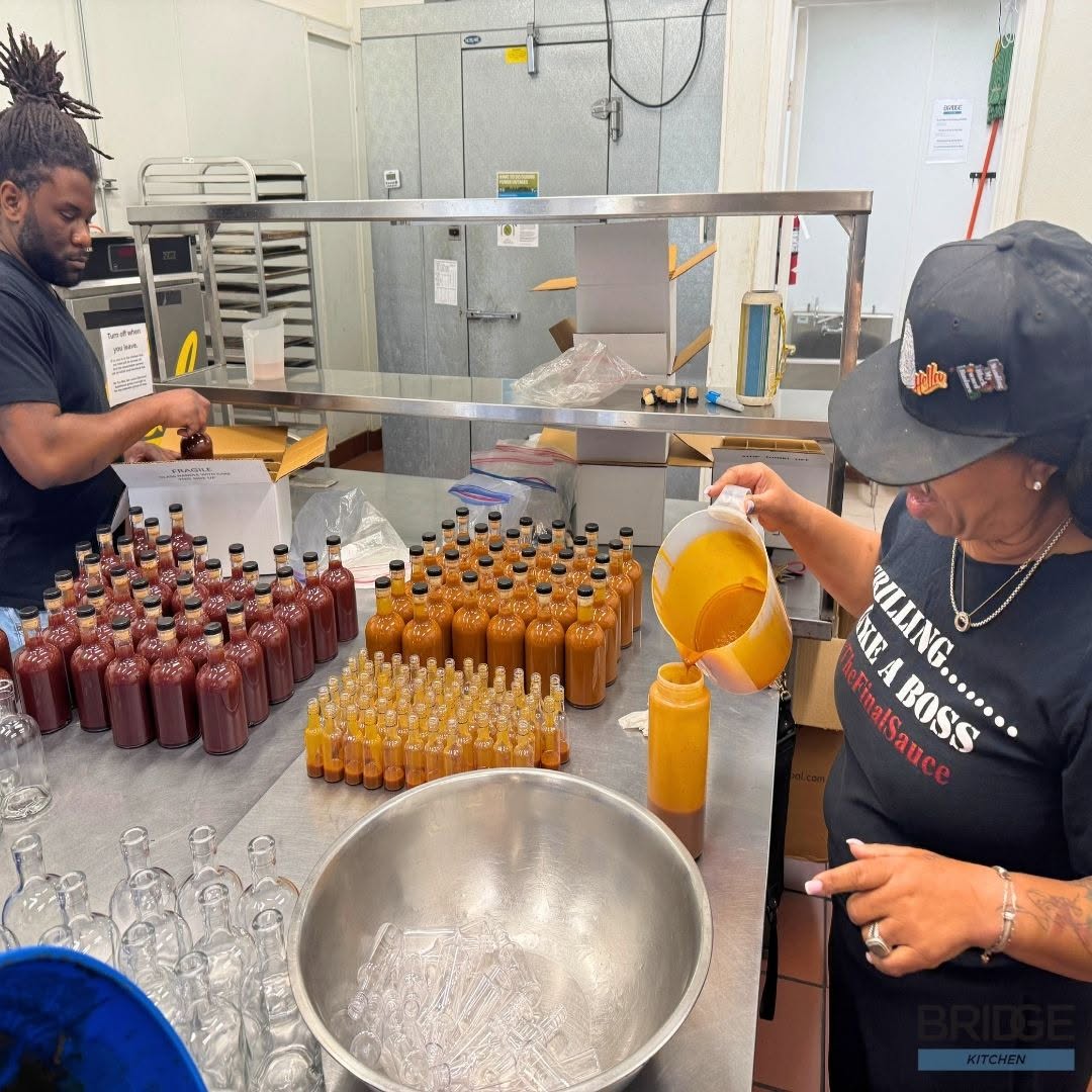Two people bottling hot sauce in the Bridge commercial kitchen