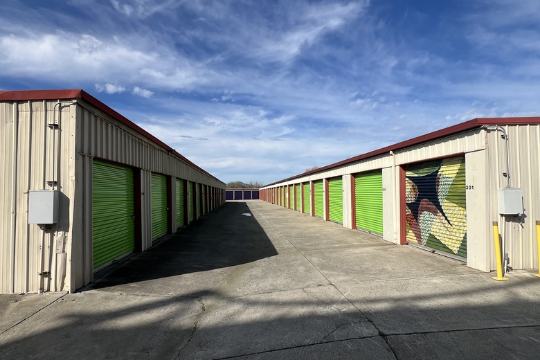 A clean outdoor aisle of green drive-up storage units under blue sky